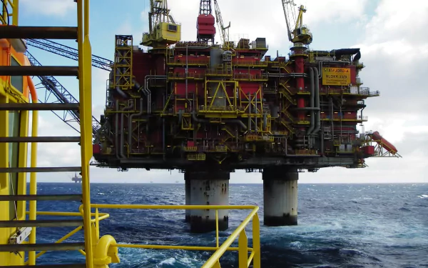 HD PC desktop wallpaper and background showing a man-made offshore oil platform rising from the sea, seen from a yellow-railed walkway beneath a cloudy sky.