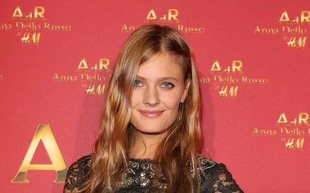 HD desktop wallpaper of a French female model with long blonde hair in a black lace dress, smiling against a red event backdrop.