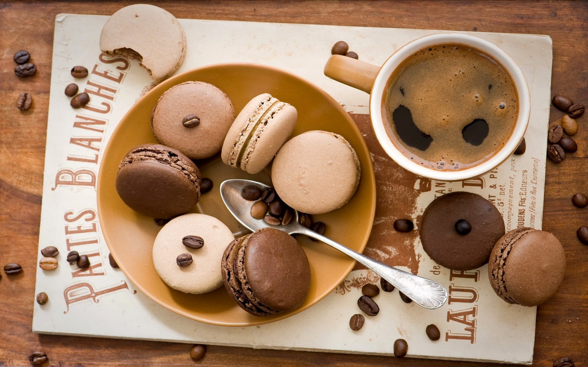 HD PC desktop wallpaper featuring a plate of assorted macarons with coffee and scattered coffee beans on a rustic wooden surface.