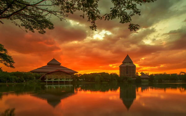 Sunset over the University of Indonesia campus showcasing traditional architecture reflected on calm water, captured in an HD man-made desktop wallpaper.