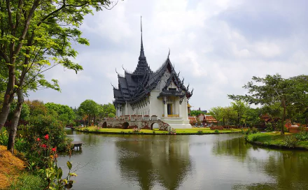 HD desktop wallpaper featuring the Sanphet Prasat Palace in Thailand, surrounded by lush greenery and a reflective pond under a cloudy sky.
