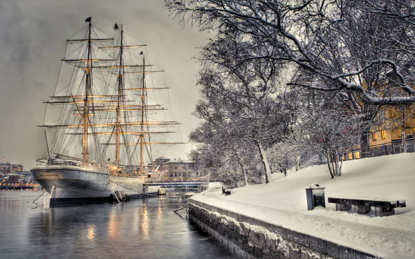 A majestic sailboat docked by a snowy riverside, illuminated against a wintry backdrop, making an inspiring HD desktop wallpaper and background.