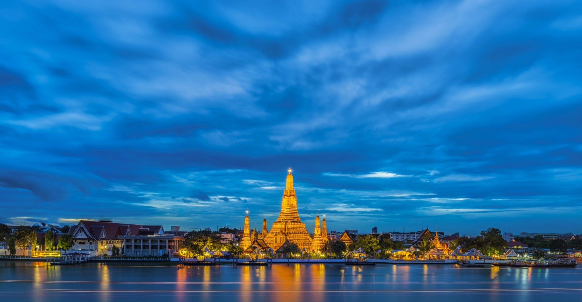 Wat Arun temple at dusk on the Chao Phraya River, Bangkok, Thailand — 2K Quad HD PC desktop wallpaper background with illuminated spires reflected in the water.