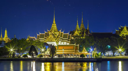 Night view of Bangkok’s Grand Palace in Thailand, illuminated with golden lights reflecting on the calm river, captured in high-definition for a desktop wallpaper background.