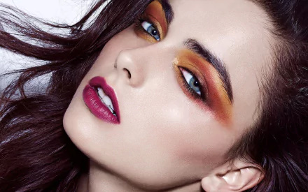 Close-up HD desktop wallpaper of model Darla Baker’s face showcasing bold orange and yellow eye makeup and deep berry lipstick.