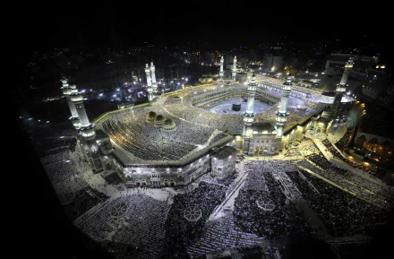 An aerial view of Masjid al-Haram in Mecca at night, featuring the Kaaba surrounded by worshippers, illuminated minarets, and a vibrant atmosphere of devotion.