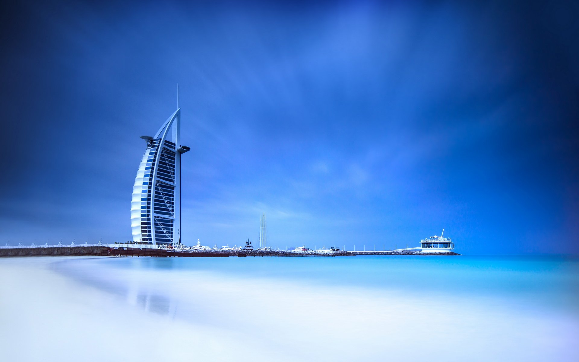 HD desktop wallpaper featuring the Burj Al Arab, a man-made architectural icon set against a serene blue sky and calm sea.