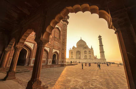 HD desktop wallpaper of the Taj Mahal in Agra, Uttar Pradesh, India, viewed through the arches of a nearby structure. The man-made marvel stands majestically in a warm, golden sunset.
