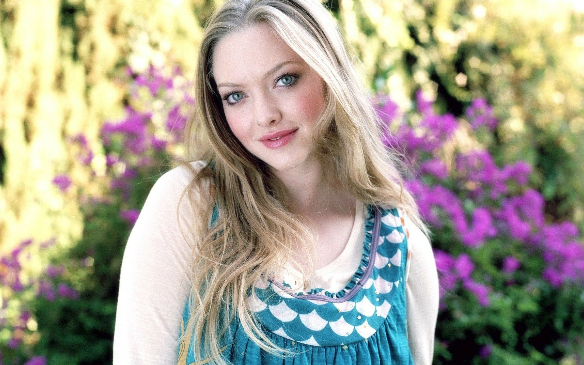 HD desktop wallpaper featuring celebrity Amanda Seyfried with a soft smile, set against a vibrant floral background.