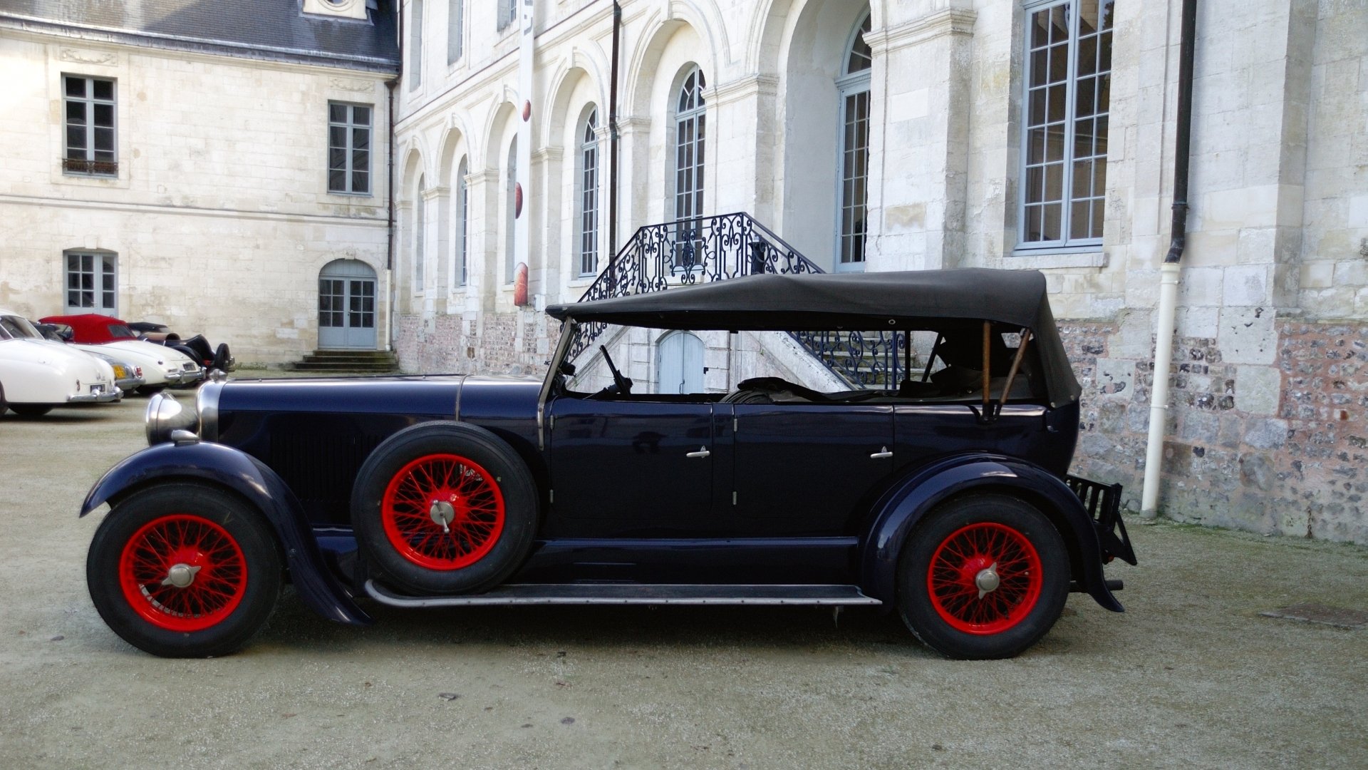HD PC desktop wallpaper/background: side view of a vintage vehicle — a dark blue Lagonda 16/80 with red wire wheels parked in front of a classical stone building.