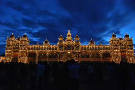A stunning view of Mysore Palace in Karnataka, India, depicted at night with vibrant lighting against a dramatic sky, showcasing its magnificent architecture.