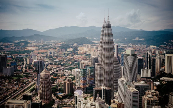 A breathtaking view of the Petronas Towers in Kuala Lumpur, Malaysia, showcasing its iconic architecture amidst a bustling city skyline and mountains in the background.
