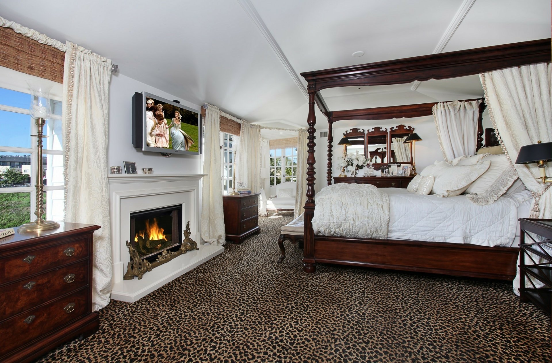 HD PC desktop wallpaper showing a spacious bedroom with a four-poster bed, a fireplace, a wall-mounted TV set, and large windows with white curtains.