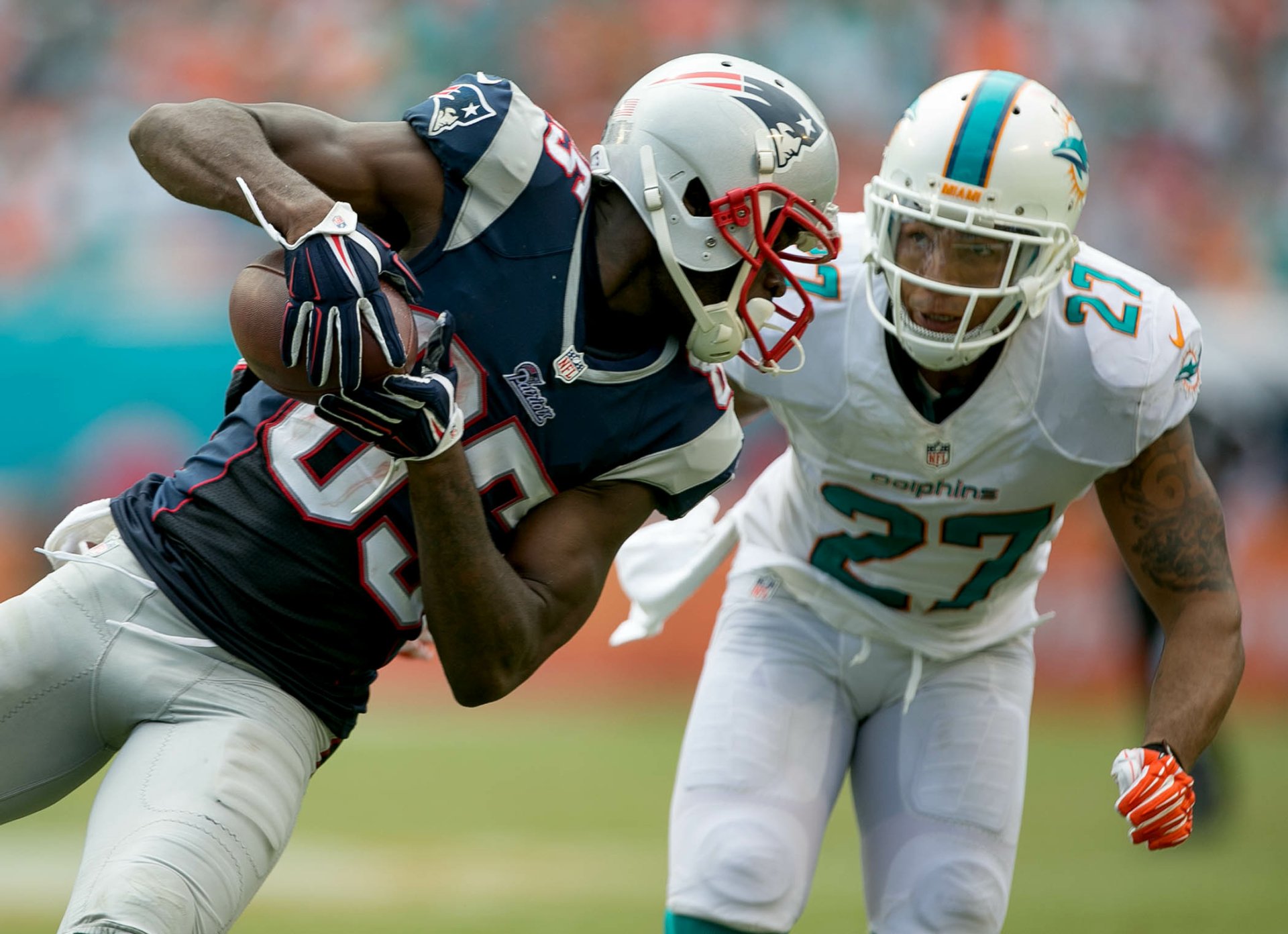 HD desktop wallpaper featuring a Miami Dolphins player defending against a New England Patriots receiver during an intense NFL game.