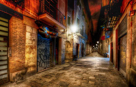 HDR image of a narrow, empty street in Barcelona, Spain, showcasing man-made historic buildings illuminated by streetlights at night, captured in HD quality for a desktop wallpaper.