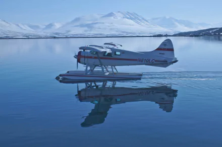 A De Havilland DHC-2 Beaver seaplane floats gracefully on calm waters, reflecting snow-capped mountains in wintery Sweden, creating a serene and picturesque scene.