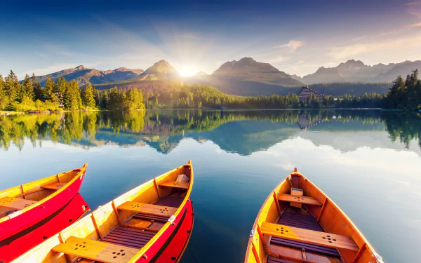 Sunshine over a serene lake in Slovakia's High Tatras, with wooden boats in the foreground and mountains reflected on the water, captured in HD quality.