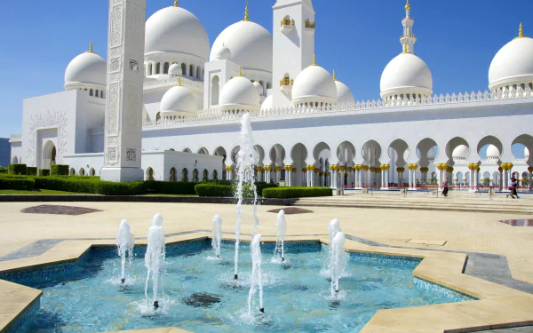 HD desktop wallpaper showing the Sheikh Zayed Grand Mosque in Abu Dhabi, United Arab Emirates, featuring a beautiful fountain in the foreground under a clear blue sky.