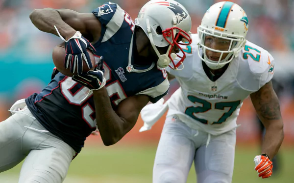 HD desktop wallpaper featuring a Miami Dolphins player defending against a New England Patriots receiver during an intense NFL game.