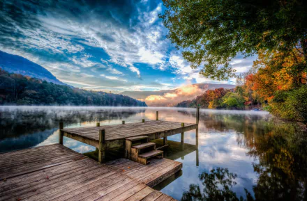 HD PC desktop wallpaper photography: fog over a glassy mountain lake at sunrise, dramatic sky, wooden dock in foreground and colorful autumn shoreline.