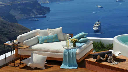 HD desktop wallpaper capturing a cozy lounge sofa with cushions overlooking the ocean, a cruise ship near Santorini, Greece, evoking a serene holiday atmosphere.