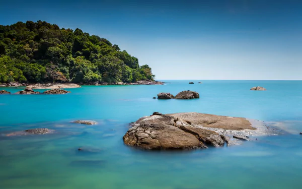 HD PC desktop wallpaper of a tropical Malaysian lagoon: turquoise sea around smooth rocks, lush green shoreline and clear blue sky.