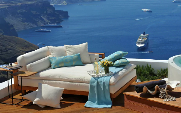HD desktop wallpaper capturing a cozy lounge sofa with cushions overlooking the ocean, a cruise ship near Santorini, Greece, evoking a serene holiday atmosphere.