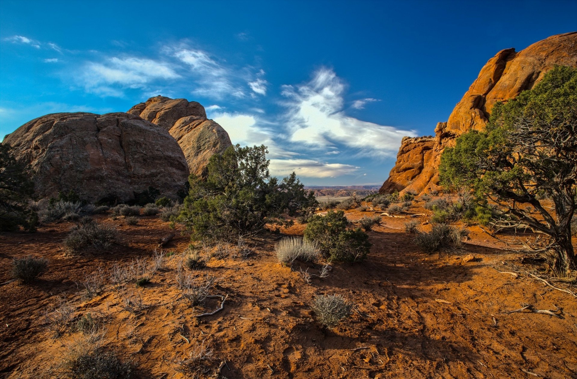HD PC desktop wallpaper showcasing a vibrant desert landscape with rocky formations, sparse vegetation, and a bright blue sky with scattered clouds.