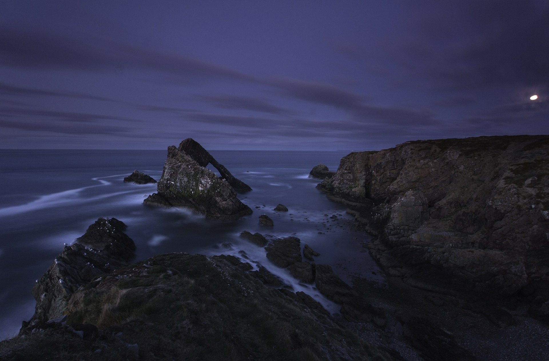 HD PC desktop wallpaper capturing a serene twilight seashore with rugged rocks and calm ocean waves under a deep blue sky.