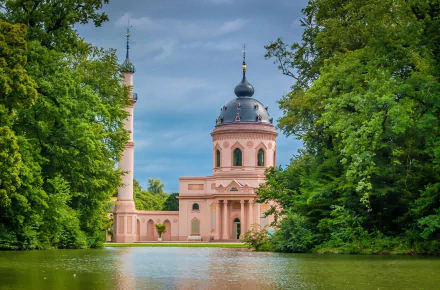 View of the Pink Mosque surrounded by trees and a lake in Schwetzingen, Baden-Württemberg, Germany, showcasing the religious building and its serene landscape.