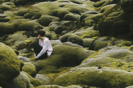 HD PC desktop wallpaper background — a solitary woman seated among moss-covered rocks, the soft green landscape conveying a quiet, introspective mood.