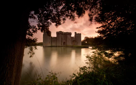 Man-made Bodiam Castle at dusk, framed by trees and mirrored in its calm moat — HD PC desktop wallpaper.
