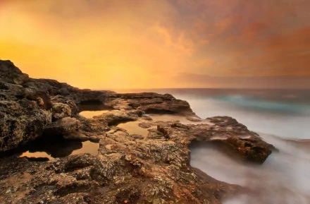 HD PC desktop wallpaper/background: golden sunset over a rocky seashore, waves flowing into the sea beneath a warm, glowing sky — serene nature scene.