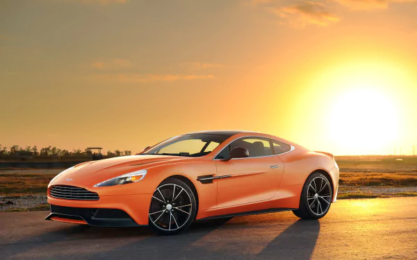 Orange Aston Martin Vanquish sports car at sunset on an open road — 4K Ultra HD PC desktop wallpaper background.