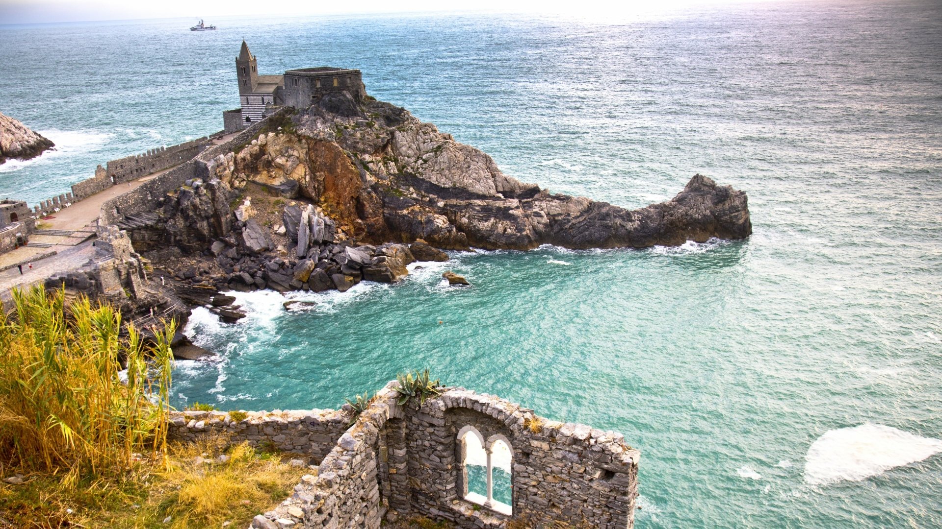 4K Ultra HD desktop wallpaper of Porto Venere's rugged coastline with historic stone church and fort perched on a rocky promontory, turquoise sea and ruined stone arch in foreground.
