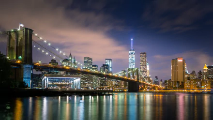 HD desktop wallpaper showcasing the Brooklyn Bridge with the Manhattan skyline illuminated at night, reflecting on the water.