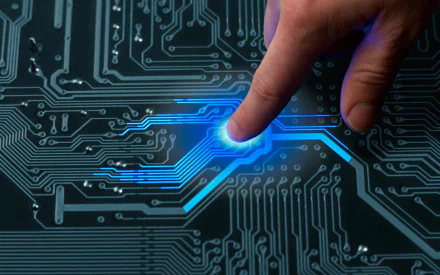 A close-up of a hand pressing a glowing point on a circuit board, showcasing intricate technology design. This HD image serves as a striking desktop wallpaper and background.