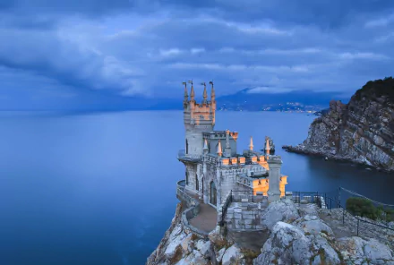 HD desktop wallpaper of the Swallow's Nest, a man-made castle perched on a cliff overlooking the Black Sea in Yalta, Russia, under a cloudy blue sky.