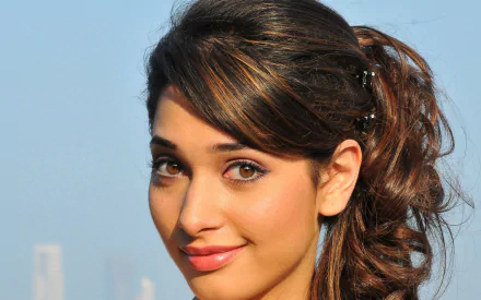 HD desktop wallpaper featuring a close-up face portrait of Bollywood celebrity Tamannaah Bhatia against a clear sky background.