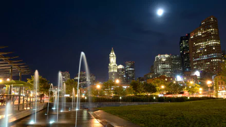 A vibrant night scene in Boston, featuring illuminated skyscrapers and fountains, with a full moon shining brightly over the cityscape. Captured in stunning 4K Ultra HD.