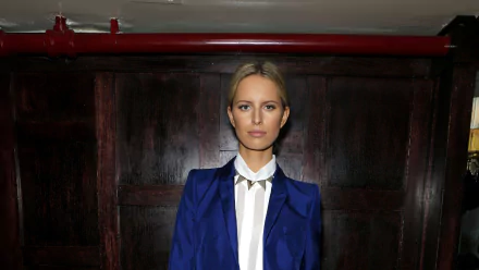 Portrait of a blonde woman in a royal blue blazer and white blouse framed against dark wooden panels, 2K Quad HD desktop wallpaper.