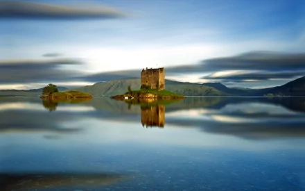 HD PC desktop wallpaper showing Castle Stalker, a man-made stone castle on a tiny island mirrored in calm loch waters beneath a sweeping sky.