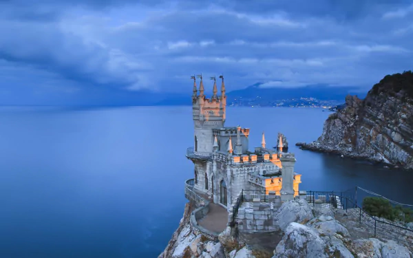 HD desktop wallpaper of the Swallow's Nest, a man-made castle perched on a cliff overlooking the Black Sea in Yalta, Russia, under a cloudy blue sky.