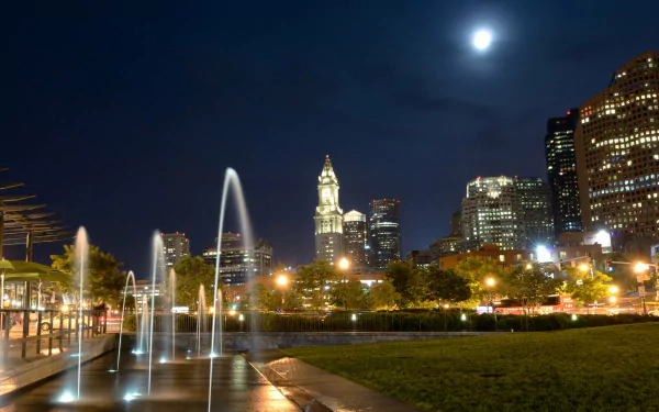 A vibrant night scene in Boston, featuring illuminated skyscrapers and fountains, with a full moon shining brightly over the cityscape. Captured in stunning 4K Ultra HD.