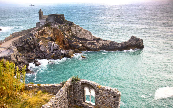4K Ultra HD desktop wallpaper of Porto Venere's rugged coastline with historic stone church and fort perched on a rocky promontory, turquoise sea and ruined stone arch in foreground.