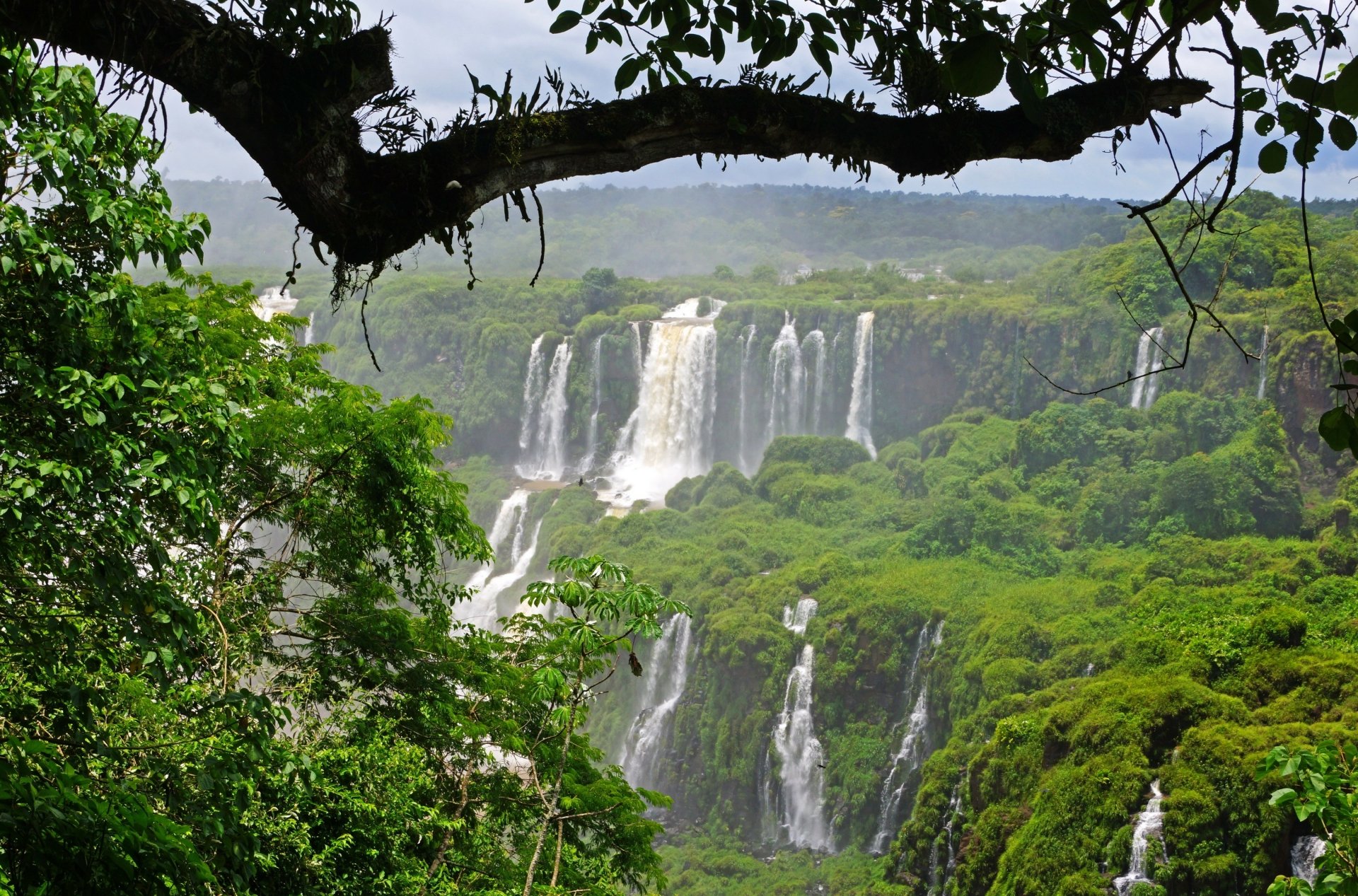 A breathtaking view of Iguazu Falls, surrounded by lush greenery in Brazil, showcasing the mist and power of cascading water amidst a vibrant natural landscape.