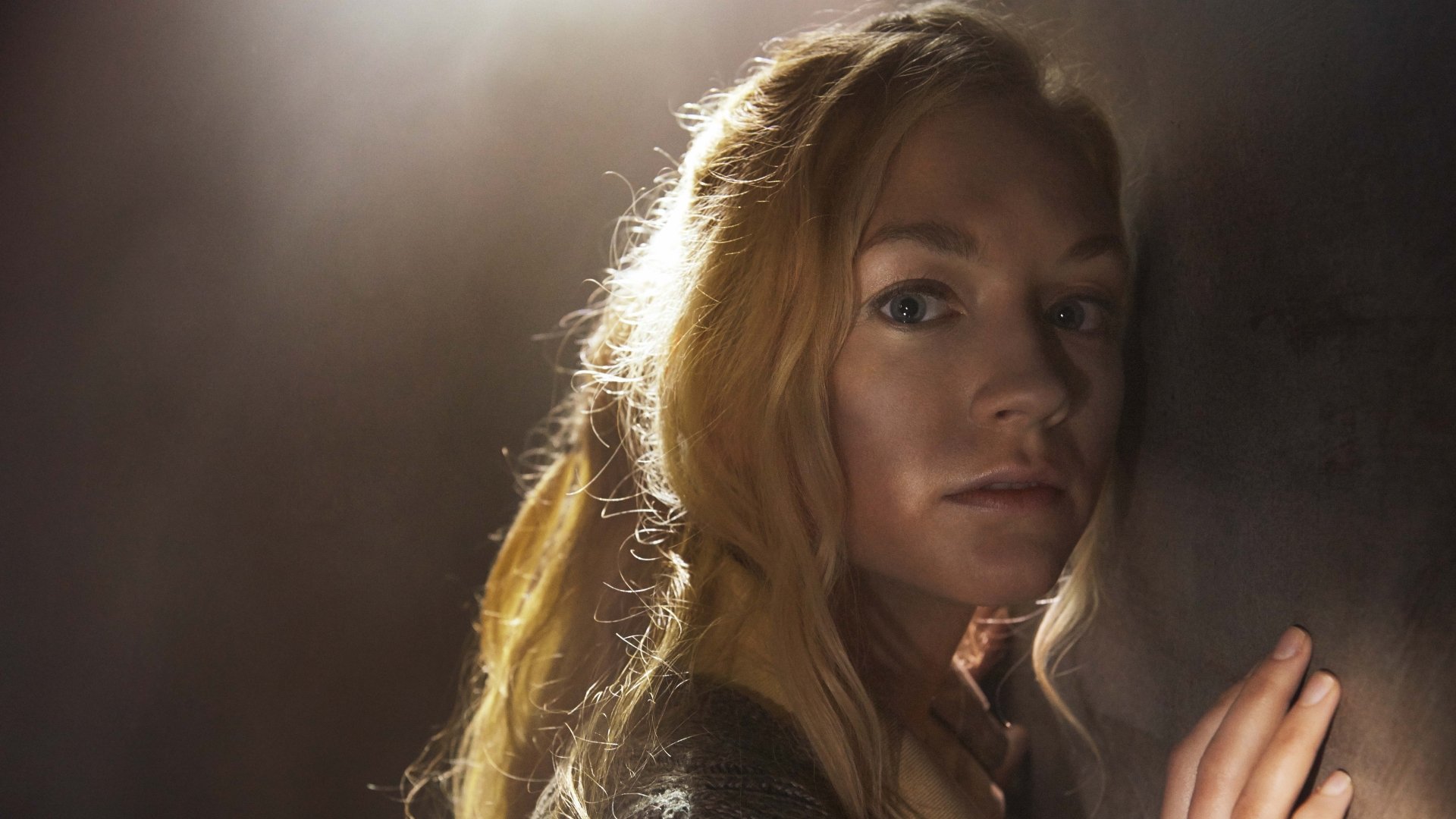 A close-up of a woman with long blonde hair, looking intensely towards the camera, set against a moody background from the TV show The Walking Dead, displayed in 4K Ultra HD.