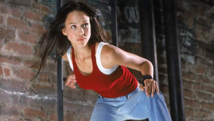 HD PC desktop wallpaper from the TV show Dark Angel: a woman in a red tank top and jeans in an action pose against a brick wall, poised to leap.