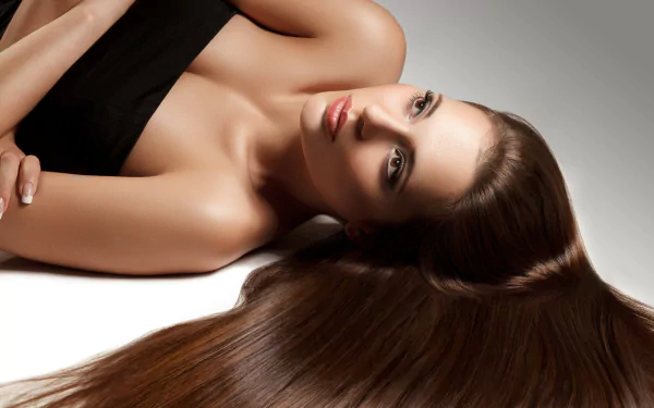 A close-up of a woman with long, flowing hair, posed elegantly on a smooth surface. This 4K Ultra HD image showcases her striking features and glossy locks.