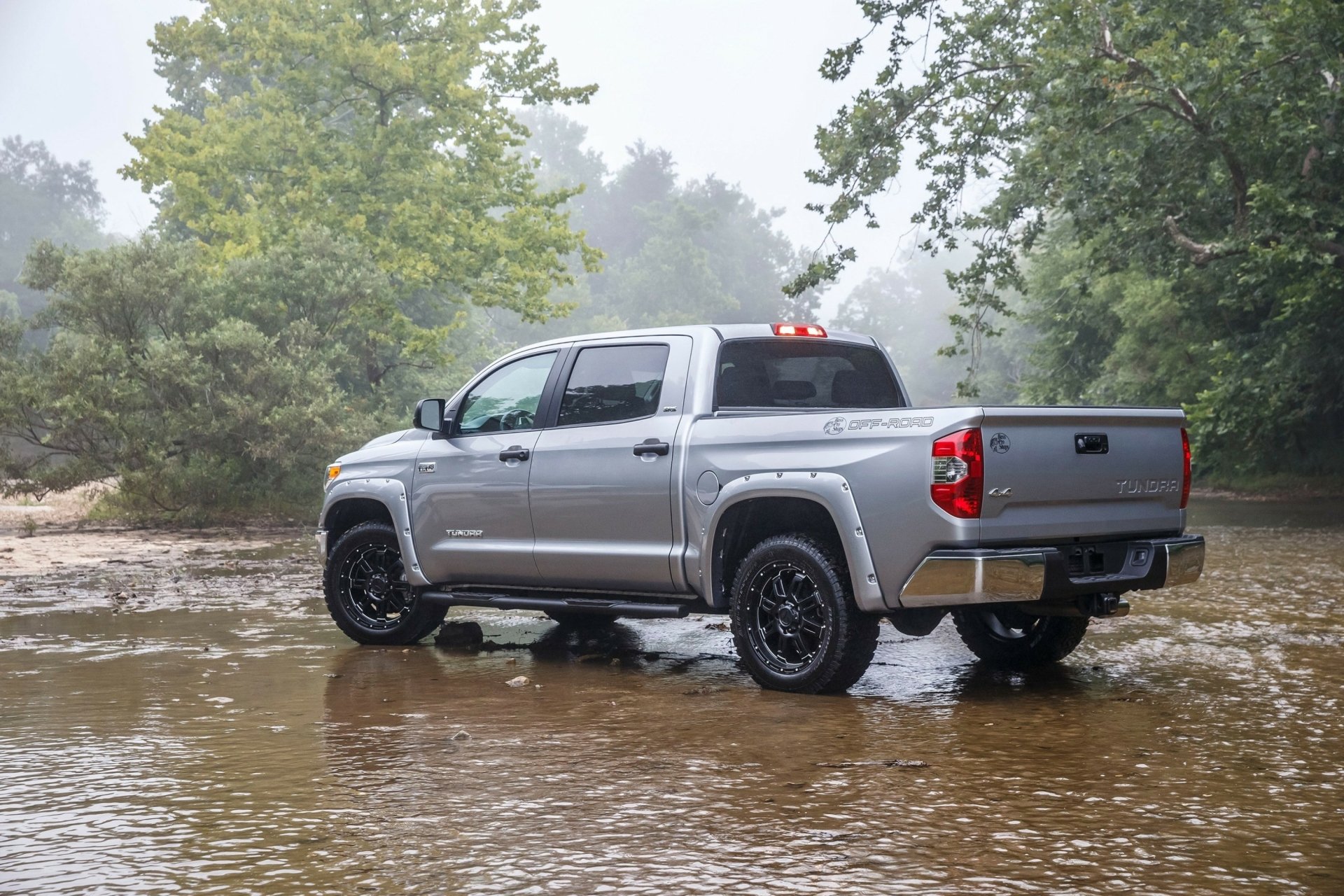 Silver Toyota Tundra vehicle in shallow river amid fog and trees — 2K Quad HD PC desktop wallpaper/background.